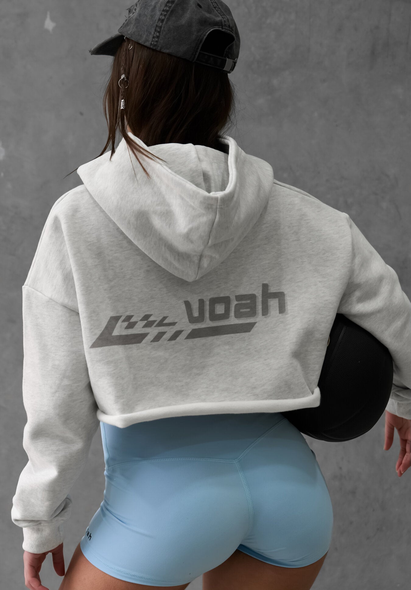 Person wearing a gray hoodie with 'voah' branding and light blue shorts against a gray background